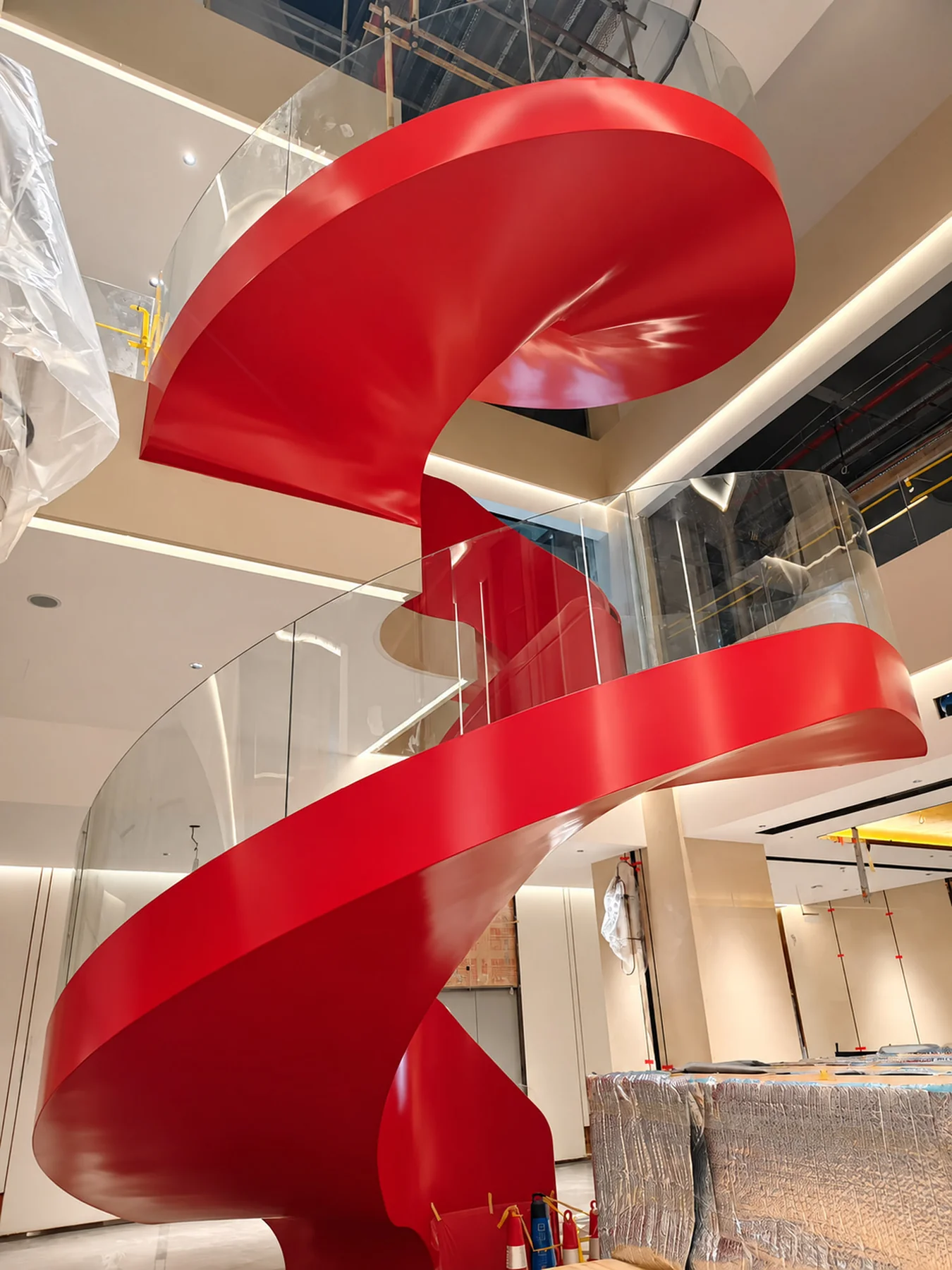 Red curved steel staircase with glass guarding at Jiahua Hotel in Chenzhou, China, with fit-out work and protective coverings visible.