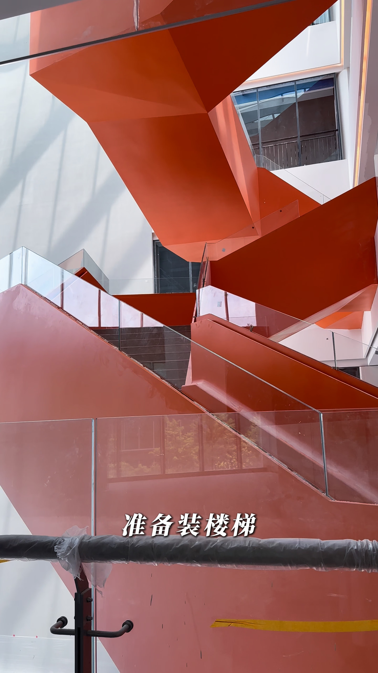 红色多跑楼梯侧面、底面与玻璃栏板的施工阶段参考，前景仍有包覆横杆