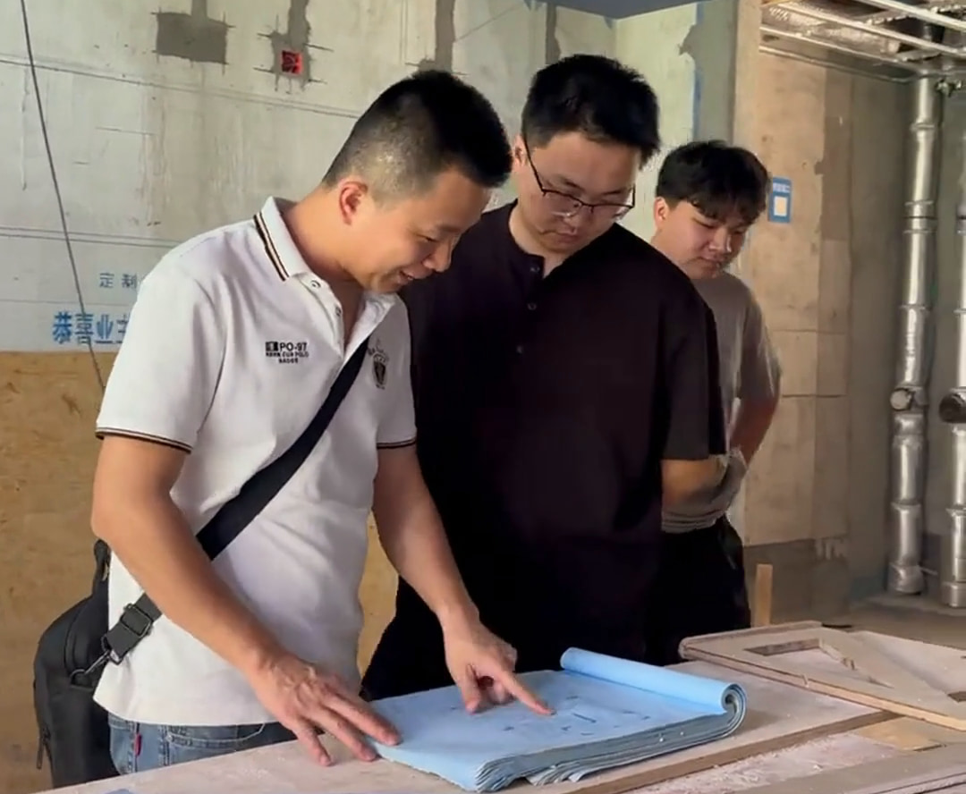 三位人员在施工现场查看桌上的蓝色图纸