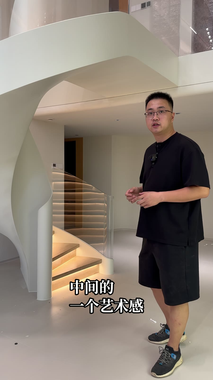 人物站在楼梯起步旁，内侧浅色钢板曲线与上方侧板相连，外侧透明栏板后可见亮起的踏步。