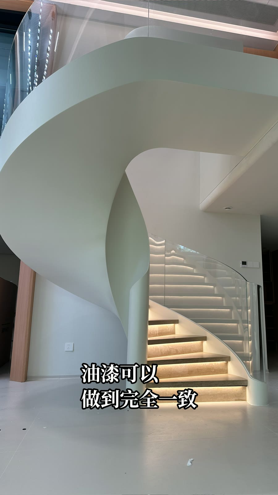 从楼梯下方看浅色封闭底面与弧形侧板，右侧可见玻璃栏板和带灯光的踏步。